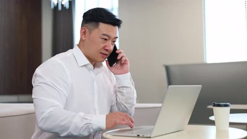 Man Talking on Phone While Working on Laptop