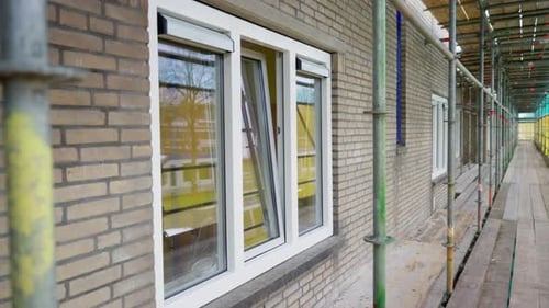 Vue extérieure d'un bâtiment en brique en rénovation avec échafaudage et fenêtre blanche.