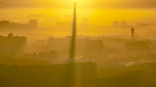 City skyline shrouded in dense golden smog and sun rays at sunrise