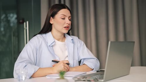 Woman Talking on Laptop Video Call While Taking Notes