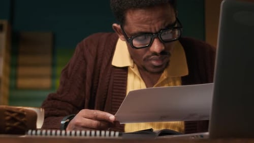 Man Reviews Documents with Laptop at Desk