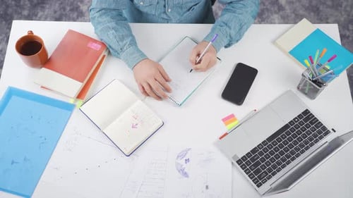 Person Writing At Desk With Laptop and Notebook