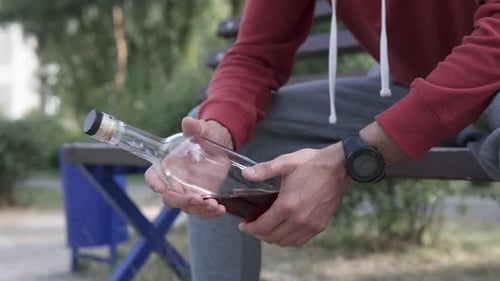 Man Holding Bottle of Red Liquid on Park Bench