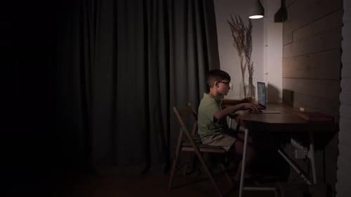 Junge mit Brille konzentriert sich auf seine Schularbeiten oder Online-Lernen, indem er auf einem Laptop tippt