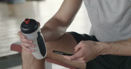 Portrait of a guy in a gym while resting between a workout and the other uses his phone to watch s