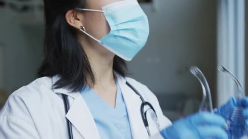Asian female nurse wearing face mask putting on protective safety glasses in hospital