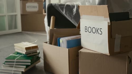 Pile de livres attachés et trois boîtes de déménagement sur le sol recouvert de moquette dans le salon