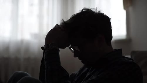 Silhouette of Troubled Young Man in Dark Room