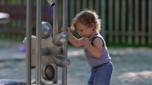 Toddler playing with metal sand funnel equipment at playground pouring sand between bowls