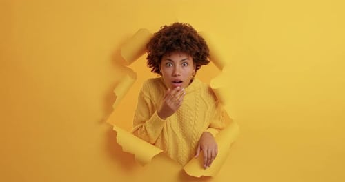 Surprised woman with curly hair bursting through paper