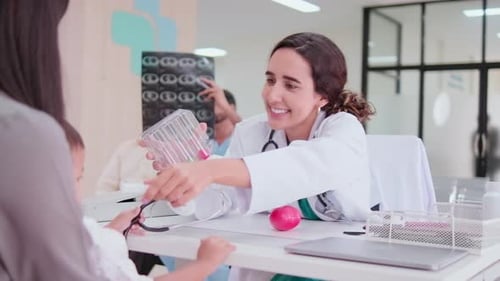 Female pediatric doctor teasing boy with toy for medical examination.