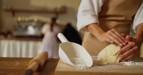 Closeup of a Girl Baker in a White Shirt and Beige Apron Prepares Dough Using Flour on a Cutting