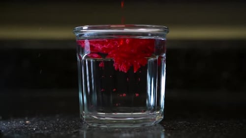 Cire rouge fondue à chaud versée dans un verre d'eau claire froid (Ralenti)