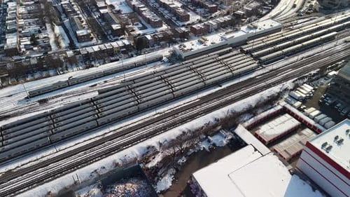 Aerial view of a large train depot with multiple tracks and passenger cars next to a snowy