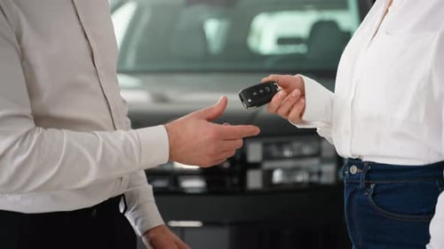 A Car Salesman Hands Over the Keys to a New Vehicle to a Female Customer in a Dealership