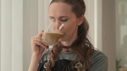 Junge Handwerkerin genießt eine Tasse Kaffee in ihrer eigenen Lederwerkstatt