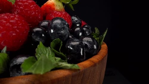 Close up rotating forest berries in a wooden bowl with black background, strawberries, blueberries,