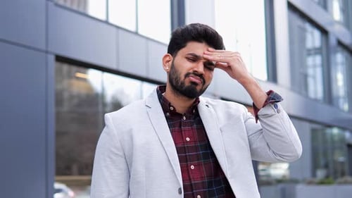 Indian Man is Experiencing Stress and Headache Standing Outside a Building