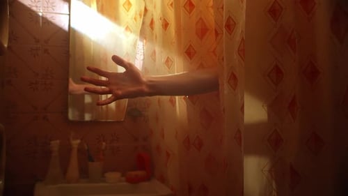 Man Holds Hand Under Sun Beam Standing Behind Shower Curtain