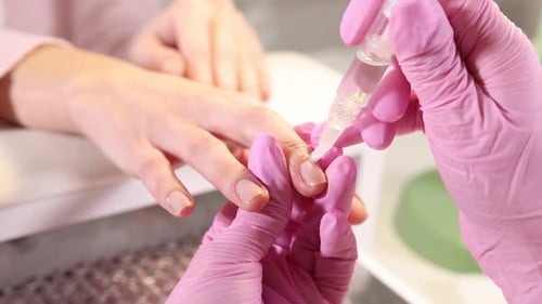 Professional manicurist applying oil onto client's nails in beauty salon, closeup