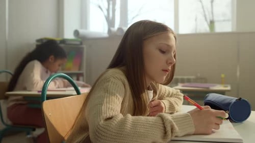 Diligent schoolgirl writing notes during lesson in modern classroom studying science