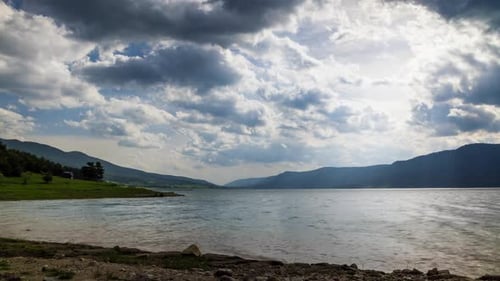 Lake with Clear Water and Stone Shore in Spruce Forest with Fir Trees Against a Daytime Sky