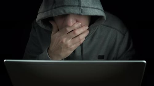 Man with Hood Using Laptop in Dark Room