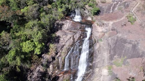Aerial view of a waterfall falling down from a steep mountain surrounded by forests.