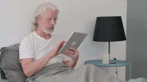 Senior Man Uses Tablet Device in Bed