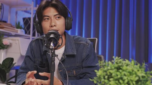 Focused podcaster speaking into microphone during livestream in blue-lit home studio