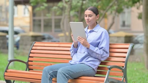 Mujer hispana que usa una tableta mientras está sentada al aire libre en un banco