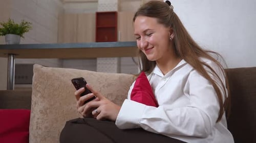 Young woman using smartphone relaxing on couch at home