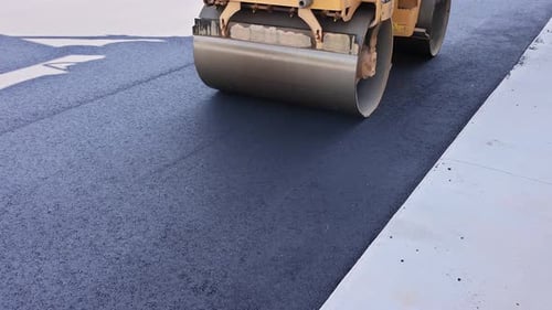Heavy Machinery Compacts Fresh Asphalt on Newly Paved Road at Busy Construction Site
