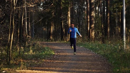Man in Athletic Gear Runs Along a Forest Trail at Sunset Enjoying an Autumn Workout That Combines