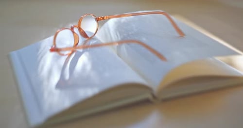 Close up of Reading Glasses and an Open Book on a Desk at Sunset