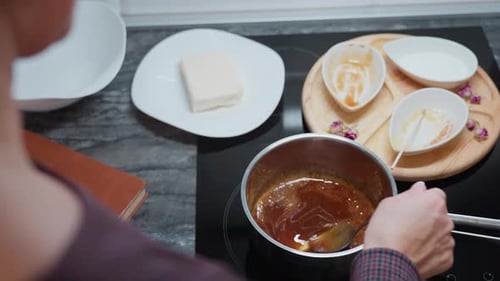 Partial View of Person Stirring Soup in Pot with Cooking Tools on Countertop