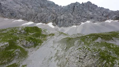 Drone flight up a mountain range of small green hills and a steep rocky wall in Tyrol, Austria