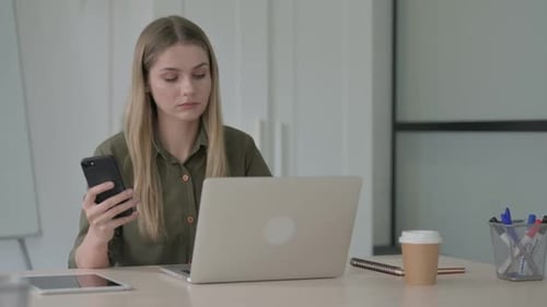 Woman Using Smartphone While Working at Laptop