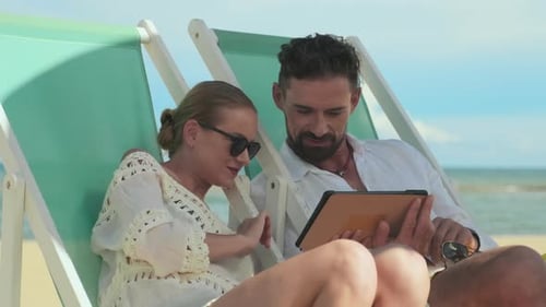 Young Man Showing His Wife New Photos in Tablet on tropical beach