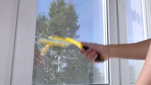 Man cleaning window with squeegee indoors, low angle view. Camera moving