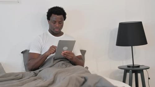 Young Adult Uses Tablet in Bed