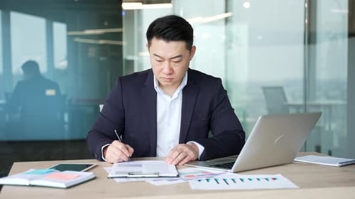 Confident asian businessman signing documents sitting at a desk at workplace in a business office.