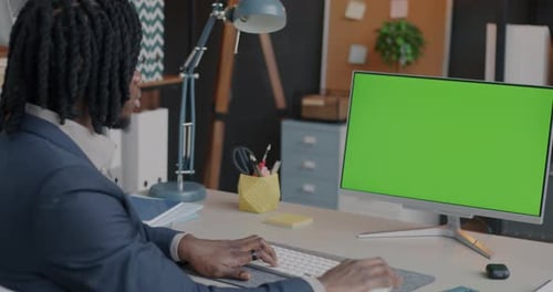African American Employee Typing with Computer Looking at Chroma Key Green Screen Monitor in Office