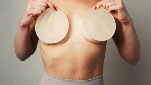 Woman Holding Silicone Breast Implants Up to Chest