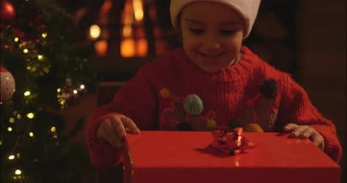 Excited Child Opens Christmas Gift by Fireplace