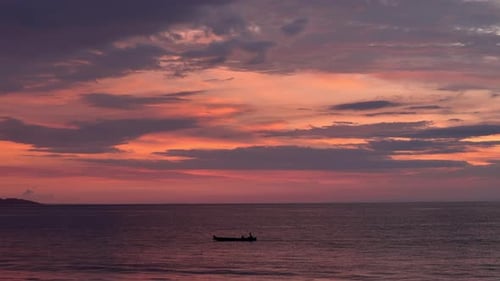 Sunset ocean with fishing boat silhouette and dramatic orange pink clouds