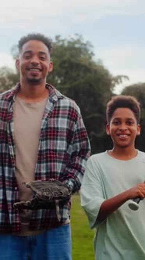 Parent and Kid Holding Baseball Tools and Looking at Camera