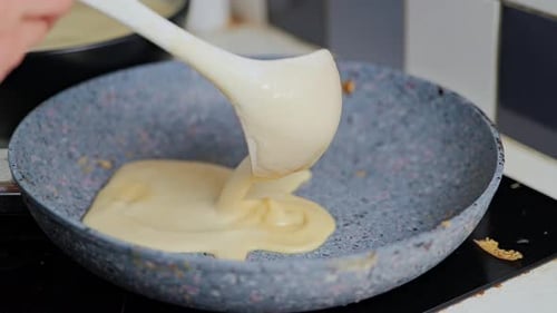 Pâte à crêpes fine faite maison versée dans une poêle dans une atmosphère de cuisine chaleureuse
