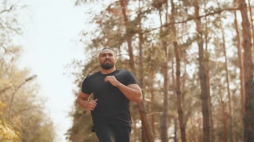 Young Muscular Jogger in Black Sportswear Running with Patience on a Path in a City Park on a Sunny