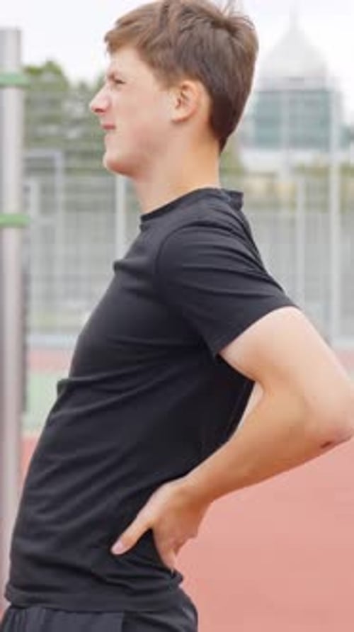 Young Man Holding Lower Back at Outdoor Gym